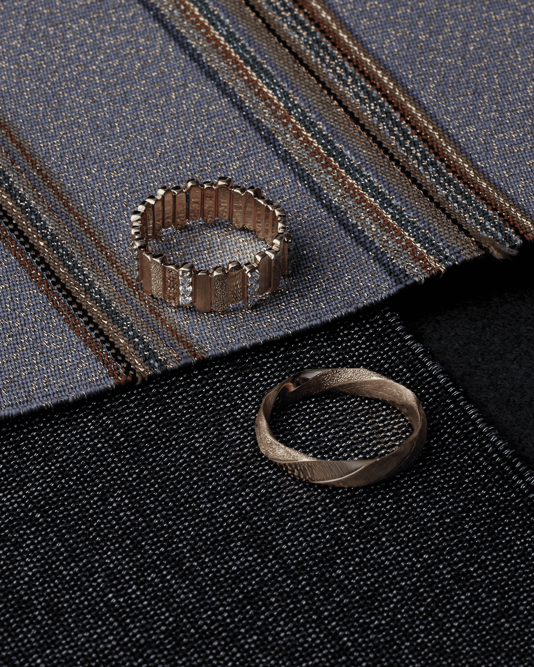 Two gold-colored rings on cloth: repeated upright units and a twisting outline.